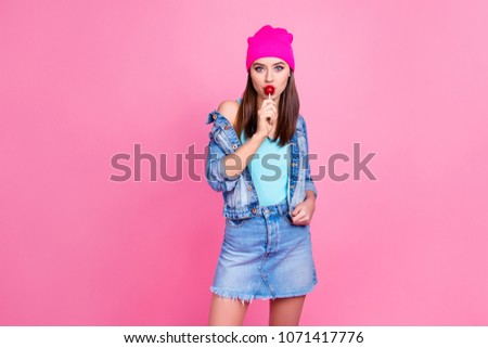 Attractive cool trendy charming girl wearing denim casual shabby ripped jeans shirt jacket pink hat enjoying the taste of lollipop, isolated on pink background, copy-space