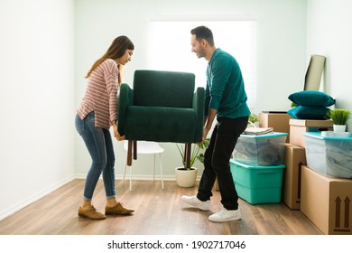 Attractive Couple Carrying Together A Stylish Chair In The Living Room. Young Woman And Man Unloading The Furniture In Their New Home Or Apartment