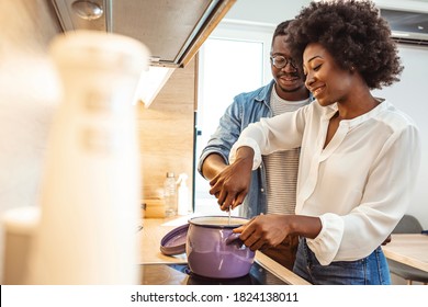 Attractive couple is cooking on kitchen. Looking on each other and smiling. Happy couple cooking dinner together in their loft kitchen at home.  Black couple cooking dinner in kitchen together. 