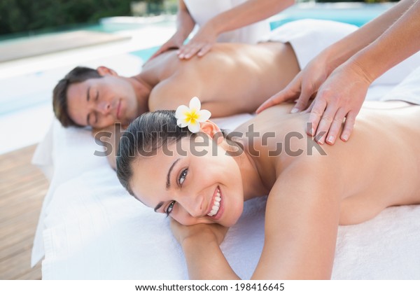 Attractive couple enjoying couples massage poolside\
outside at the spa