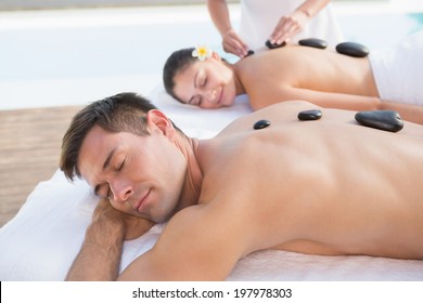 Attractive couple enjoying hot stone massage poolside outside at the spa - Powered by Shutterstock