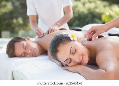 Attractive couple enjoying hot stone massage poolside outside at the spa - Powered by Shutterstock