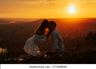 Attractive couple enjoying romantic sunset on picnic on the hill. She passionately hug his boyfriend. Romantic evening in the amazing sunset. Copy space.