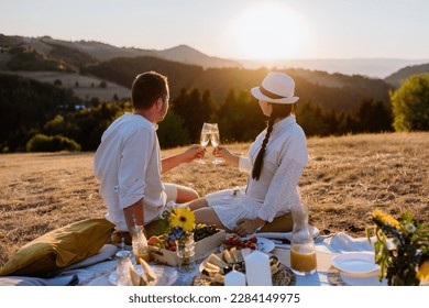 Attractive couple in love enjoying picnic and drinking wine on the hill at sunset. - Powered by Shutterstock