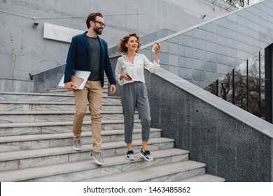 Attractive Couple Of Man And Woman Going On Stairs In Urban City Center In Smart Casual Business Style, Talking, Working Together, Smiling, Stylish Freelance People, Holding Laptop? Discussing