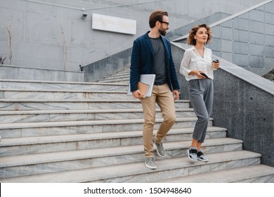 attractive couple of man and woman going on stairs in urban city center in smart casual business style, talking, working together, smiling, stylish freelance people, holding laptop? discussing - Shutterstock ID 1504948640