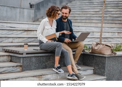 attractive couple of man and woman talking sitting on stairs in urban city center, business style, working together on laptop, smiling, stylish freelance people on meeting using technology outside - Powered by Shutterstock