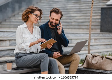 Attractive Couple Of Man And Woman Talking Sitting On Stairs In Urban City Center, Business Style, Working Together On Laptop, Smiling, Stylish Freelance People On Meeting Using Technology Outside