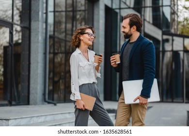 Attractive Couple Of Man And Woman Talking In Urban City Center In Smart Casual Business Style Working Together, Holding Laptop, Smiling, Stylish Freelance People, Discussing, Drinking Coffee