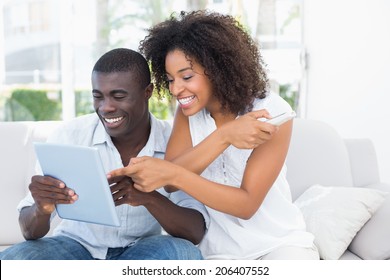 Attractive Couple Sitting On Couch Together Looking At Tablet At Home In The Living Room
