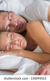 Attractive Couple Sleeping And Spooning In Bed At Home In Bedroom