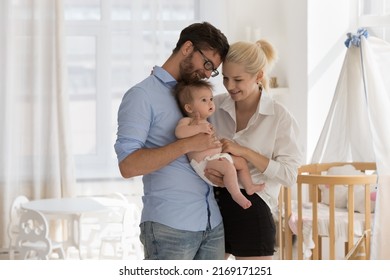 Attractive Couple, Young Loving Parents Standing Together In Cozy Nursery Holding Adorable Baby, Cuddling Cute Infant Looking Happy, Enjoy Parenthood Feeling Unconditional Love To Kid. Family Concept