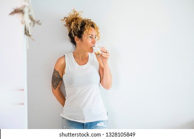 Attractive Curly Blonde Middle Age Cute Woman Drinking Water And Lemon At Home With White Wall In Background - Healthy Lifestyle For Cacuasian People - Modern Tatoo Girl