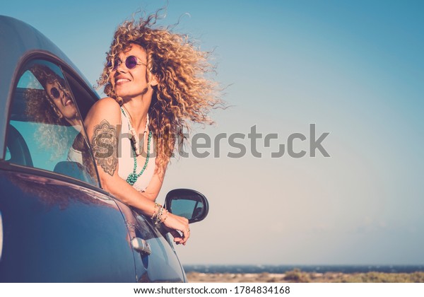 Attractive curly blonde young woman smile and enjoy\
the wind outside the car - concept of beauty and travel for happy\
and cheerful caucasian people - alternative lifestyle female feel\
the freedom joy