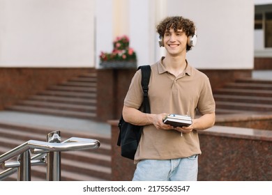 Attractive Curly Haired Young Man In Headphones With Books University Or College Student Walking On Campus