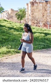 attractive curvy african american woman walking in sportswear while using her smartphone
