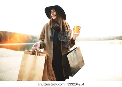 Attraktives süßes Mädchen mit Einkaufstaschen und warmen Getränken in der Hand