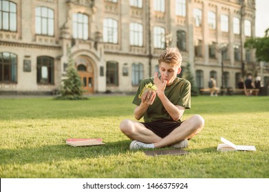 Attractive Cute Male Student Having Lunch On The College Lawn Eating Delicious Sandwich Licking His Finger. Handsome University Student Eating Appetizing Sandwich Having Rest On A Break Near Campus.