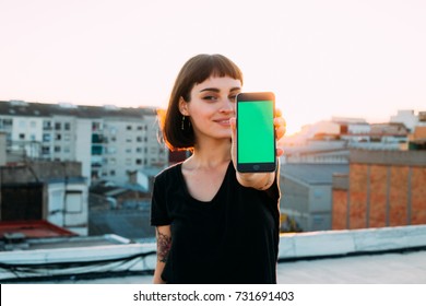 Attractive cute pretty young woman or teenager shows smartphone to camera, with green chroma key filled screen, smiles to camera, new generation millennial  - Powered by Shutterstock