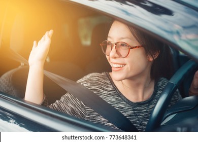 Attractive Cute Young Asian Woman In Casual Wear Looking Outside And Waving Hands In Greeting Friends Or Family While Driving A Car. Smile And Happy Time To Travel Or Rest Concept. Filtered Image