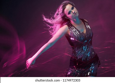 Attractive dancing blonde in the club, neon light, motion effects. Black background, long exposure