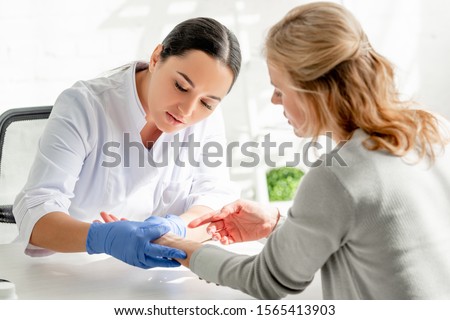 attractive dermatologist in white coat examining skin of patient in clinic