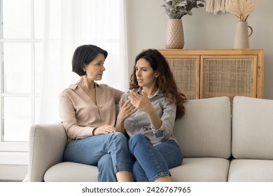 Attractive different age women, mature mom and young adult daughter lead trustworthy talk seated together on sofa, tell personal news, issues, receive support, asks advice, share life troubles at home - Powered by Shutterstock