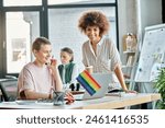 Attractive diverse businesswomen working together on project in office, pride flag.