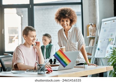 Attractive diverse businesswomen working together on project in office, pride flag.