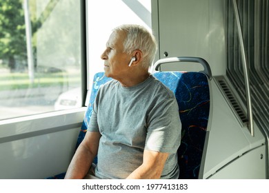 Attractive elderly man is using wireless earbuds during ride in public transport