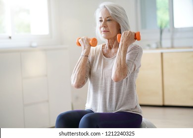  Attractive Elderly Woman Exercising At Home With Swiss Ball                              