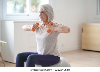  Atractiva mujer mayor haciendo ejercicio en casa con bola de baño                              