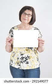 Attractive Elderly Woman Holding A Blank White Sheet Of Paper For Text.
