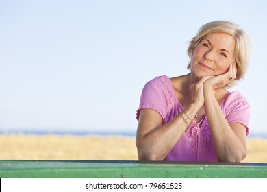 An attractive elegant and happy senior woman sitting outside out a table and thinking, behind her is a beach and the sea, s3niorlife - Powered by Shutterstock