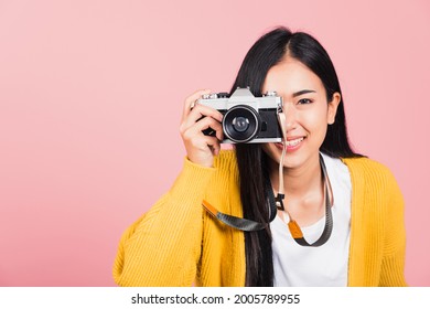 Attractive energetic happy Asian portrait beautiful young woman smiling photographer taking a picture and looking viewfinder on retro vintage photo camera ready to shoot isolated on pink background