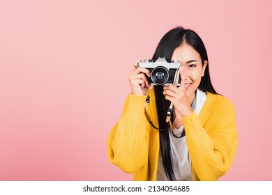 Attractive energetic happy Asian portrait beautiful young woman smiling photographer taking a picture and looking viewfinder on retro vintage photo camera ready to shoot isolated on pink background