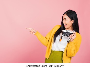Attractive energetic happy Asian portrait beautiful cute young woman teen excited smiling holding vintage photo camera and pointing finger to side space, studio shot isolated on pink background