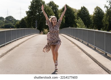 Attractive enthusiastic jubilant blond middle aged woman raising both arms to the sky in joy of success on a bridge - Shutterstock ID 2214177603