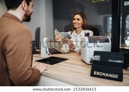 Attractive European businesswoman working in exchange office. She is giving cash money to male customer.