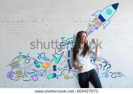 Attractive european woman celebrating success on brick wall background with creative drawn space ship. Successful young entrepreneur