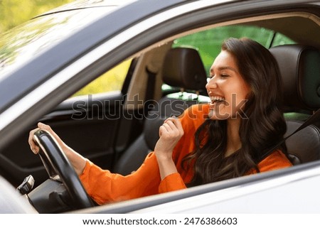 Attractive excited European woman riding her new car, having fun, enjoying listening music and singing