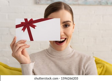 Attractive Exited Girl Covering Face With Gift Card And Looking At Camera