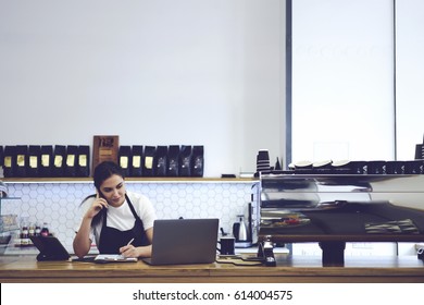 Attractive experienced barista working in cafeteria with modern design loft interior making accounting documentation in online database. Female coffee shop cashier standing against copy space wall - Powered by Shutterstock