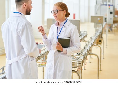 Attractive Fair-haired Factory Worker Wearing White Coat And Eyeglasses Explaining Production Process To Bearded Investor While Giving Tour Of Modern Milk Plant