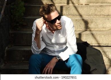 Attractive Fashion Model Sitting Down Outside Wearing A White Shirt And Black Sunglasses. 