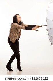 Attractive Fashionable Young Woman Struggling To Control An Umbrella On A Windy Day As It Is Caught By The Wind And Blown Away, Full Length Studio Portrait Isolated On White