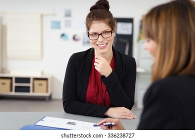 Attractive female applicant in a job interview sitting smiling happily as the interviewer reads through her curriculum vitae - Shutterstock ID 336238727