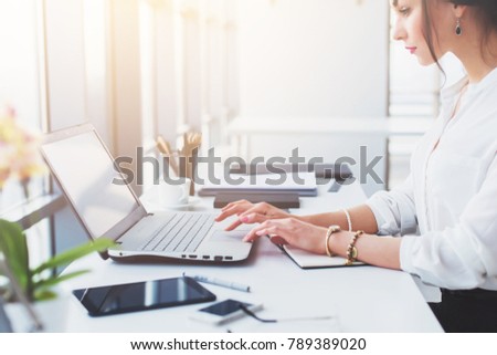 Attractive female assistant working, typing, using portable computer, concentrated, looking at the monitor. Office worker reading business e-mail.