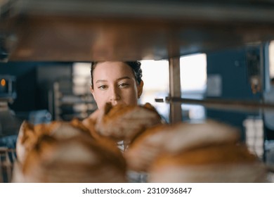 attractive female baker between shelves looking and checking freshly baked bread very carefully bakery industry - Powered by Shutterstock