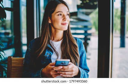 Attractive female blogger with modern smartphone gadget in hands thoughtful looking away and dreaming, youthful Caucasian blogger holding cellphone pondering thinking on idea for social publication - Powered by Shutterstock